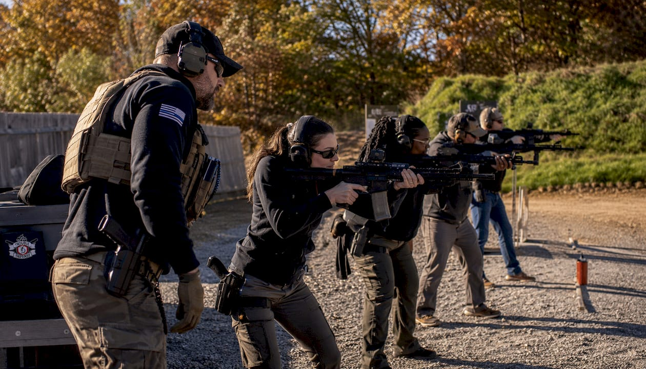 Firearm instructor coaching diverse group on outdoor range